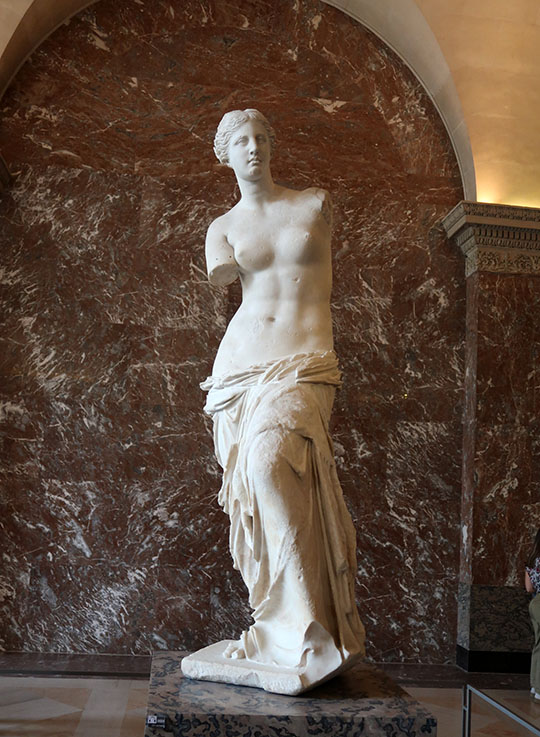 　時間有限，首先參觀羅浮宮的三寶。<br /><br />　這是羅浮宮的三寶之一的「米洛的維納斯Venus of Milos」，是一座古希臘雕像。這座雕像創作於西元前130到100年之間，表現的是希臘神話中愛與美的女神阿佛洛狄忒（羅馬神話中與之對應的女神是維納斯）。這座大理石雕成的雕像高202公分。1820年發現於希臘米洛斯島（現代希臘語稱作米洛），故被稱作米洛的維納斯。<br /> <br />　1820年，農民伊奧爾科斯在米洛斯島上發現它。他試圖將這尊雕像藏起來，但後來還是被一個土耳其軍官發現了。當時法國駐土耳其的大使將它買下，這座雕像於隔年作為禮物獻給法國國王路易十八，之後國王將其贈送給羅浮宮。<br /> <br />　米洛的維納斯以其遺失的神祕雙臂而知名。雕塑整體由兩塊大理石拼接而成，兩塊大理石連接處非常巧妙，在身軀裸露部分與裹巾的相鄰處。這座維納斯雕像是舉世公認的女性人體美的典範，這是因為她完全符合黃金分割的人體美比例關係。維納斯的造型魅力在於，無論從哪個角度去看，她都符合人體的黃金分割率，因此她能超越時代，成為女性永恆美的象徵。