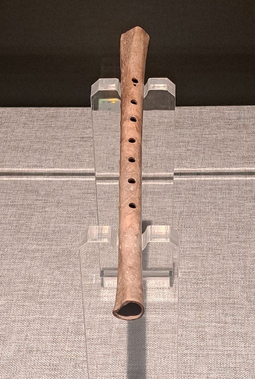 　骨笛(新石器時代)，長23.1cm，於河南省舞陽縣賈湖遺址出土。<br /><br />　距今7800年~9000年的河南賈湖遺址，是同時期最為豐富的史前聚落遺址。這裡先後出土了30多支用丹頂鶴尺骨製成的骨笛。笛孔有2、5、6、7、8之別，大多數骨笛仍為7孔。<br /><br />　賈湖骨笛是我國目前出土的年代最早的樂器實物。賈湖骨笛不只是中國年代最早的樂器實物，更被專家認定為世界上最早的可吹奏樂器。實驗證明，賈湖骨笛不僅能夠演奏傳統的五聲或七聲調式的樂曲，而且能夠演奏富含變化音的少數民族或外國樂曲。它的出土，改寫了先秦音樂史乃至整部中國音樂史，具有無可比擬的重要地位和價值。